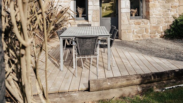 Une maison en pierre avec une terrasse en bois, une table et des chaises, et une fenêtre.