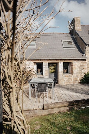 A stone house with a wooden deck, a table with chairs, and a window.