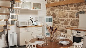Une cuisine rustique avec un mur en pierre, des poutres apparentes, des meubles blancs et une table à manger dressée pour deux personnes.