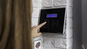 A person using a wall-mounted electronic keypad, likely for room access or security, against a textured white wall. - Smart Bnb - Hotel Battice (Herve)