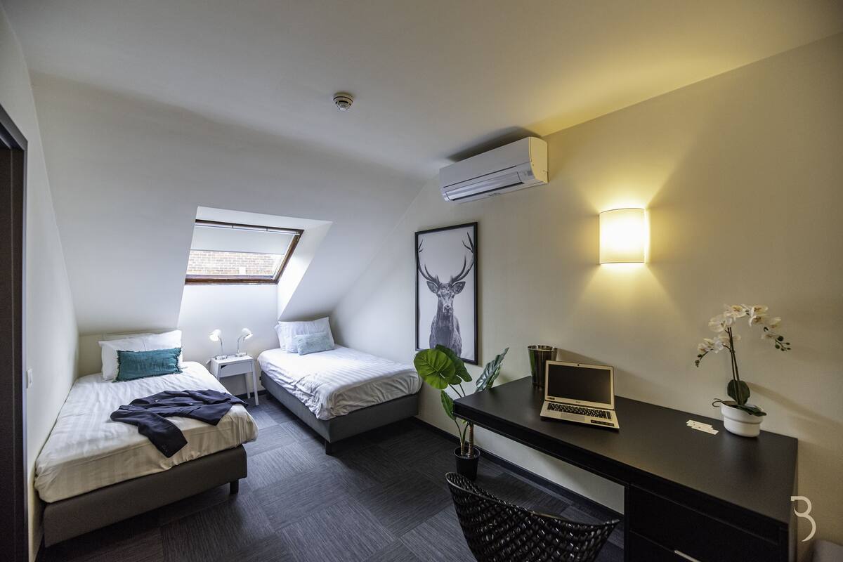 Un dormitorio moderno con dos camas, un escritorio y una computadora portátil.