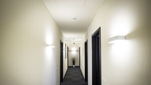 A narrow, well-lit hallway with a potted plant at the end, leading to a door. - Smart Bnb - Hotel Battice (Herve)