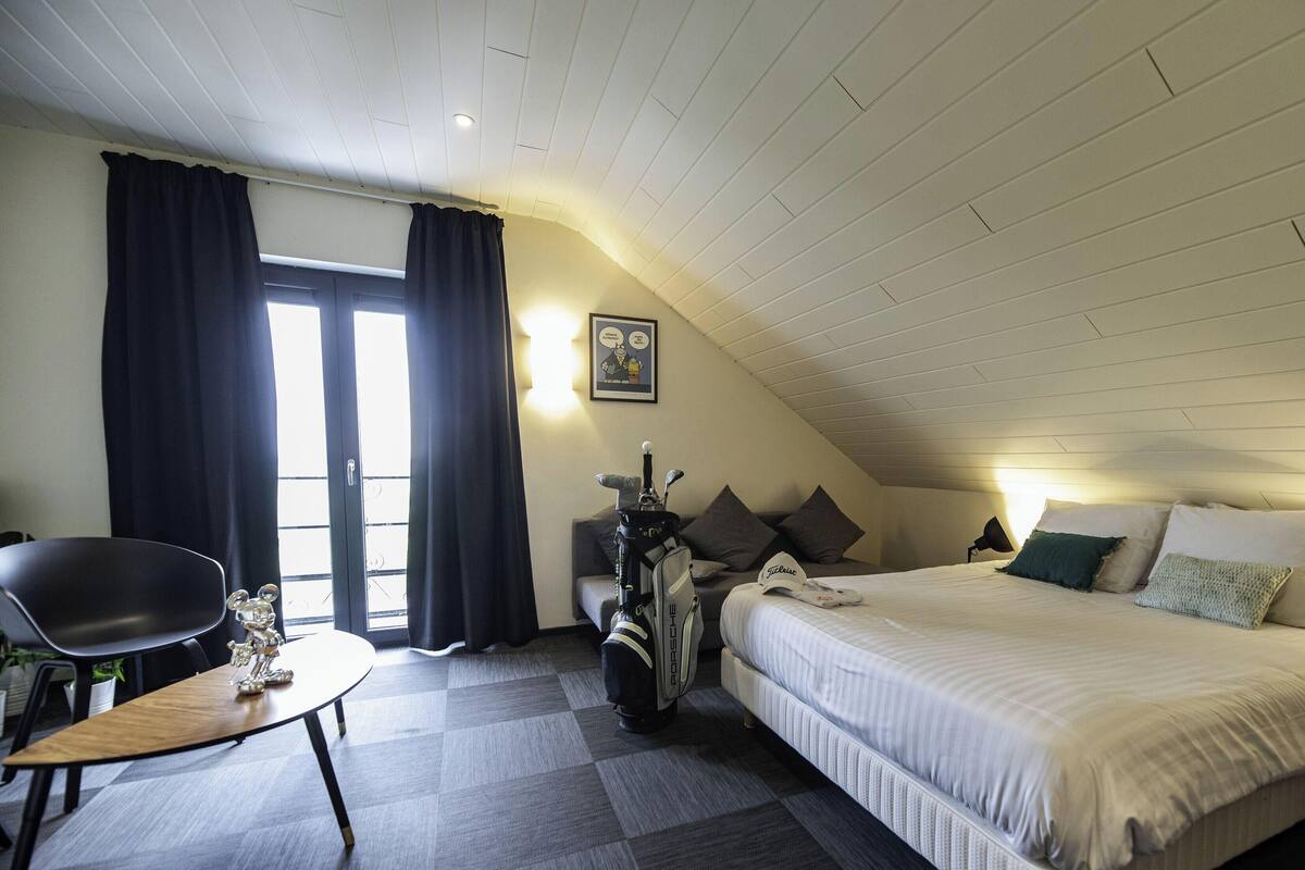 Un dormitorio con cama, escritorio, silla, bolsa de golf y ventana con cortinas.
