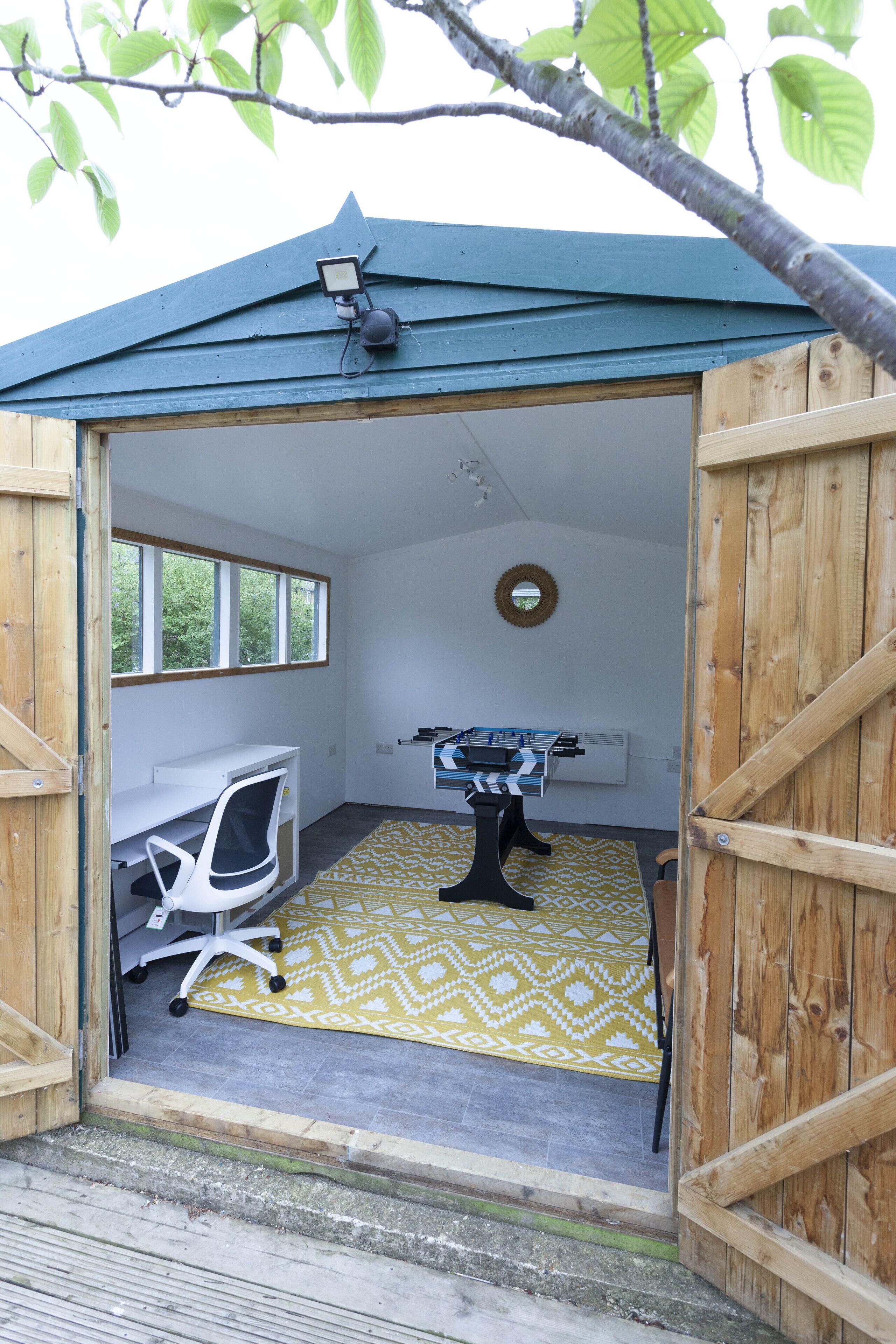 Une petite structure en bois, ouverte, comprenant un bureau, une chaise et une table de baby-foot.