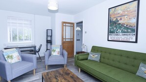 A living room with a green sofa, two armchairs, a wooden coffee table, and a painting of Whiststable & Tankerton. - Magnolia Cove with 2 parking spaces (Whitstable)