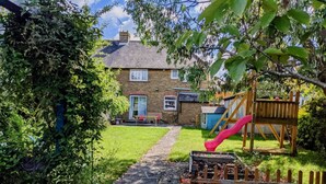 A brick house with a garden, a red slide, and a wooden fence. - Magnolia Cove with 2 parking spaces (Whitstable)