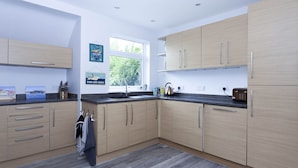 A modern kitchen with light wood cabinets, a black countertop, and a window providing natural light. - Magnolia Cove with 2 parking spaces (Whitstable)