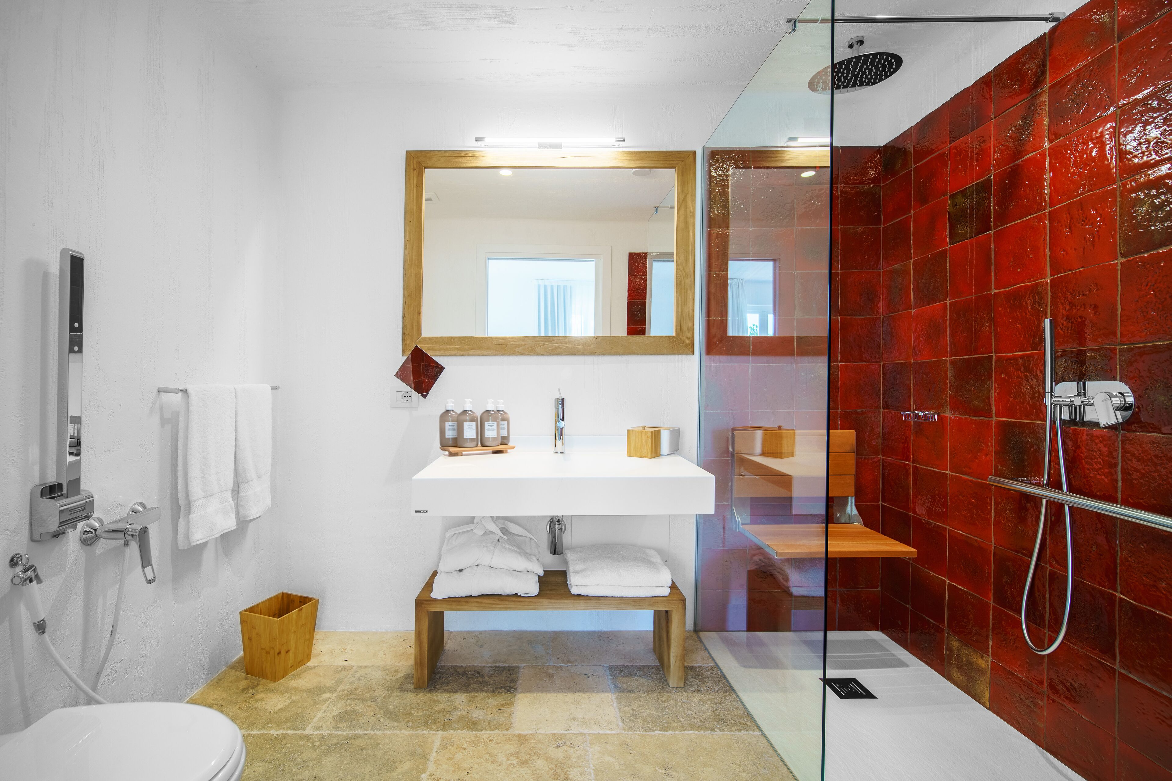 A modern bathroom with a glass shower enclosure, a white sink with a mirror above it, and a wooden bench.