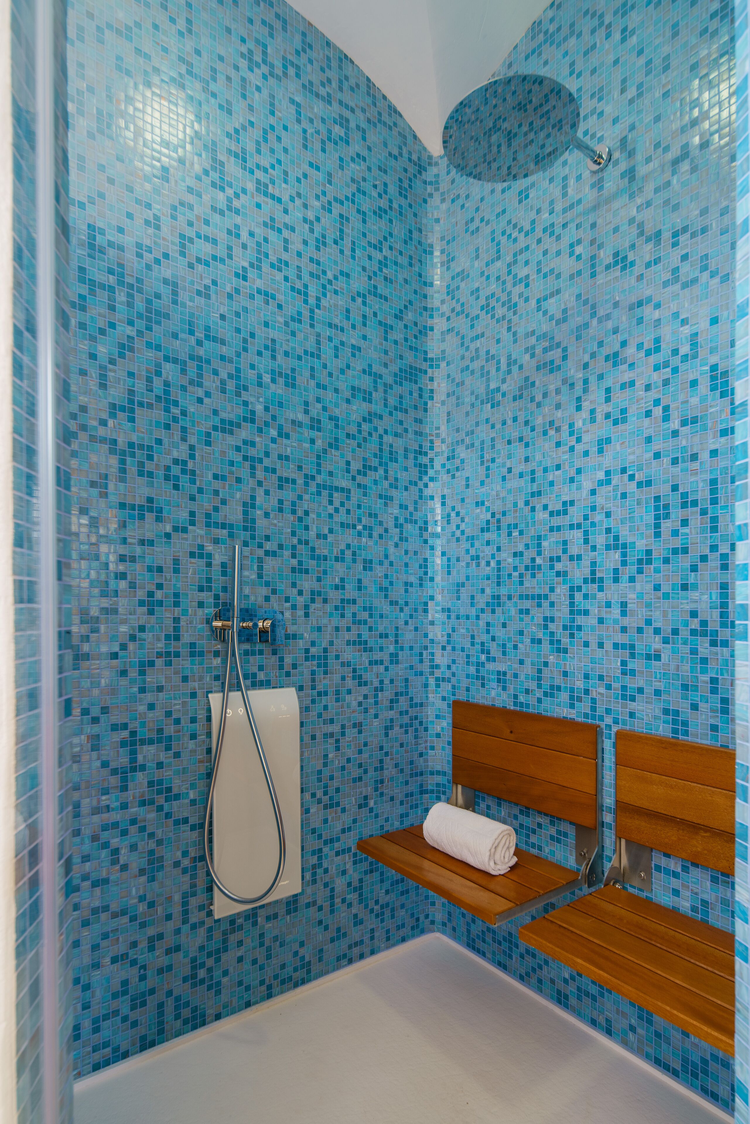 A bathroom with a mosaic tile wall, a shower, a wooden bench, and a towel rack.