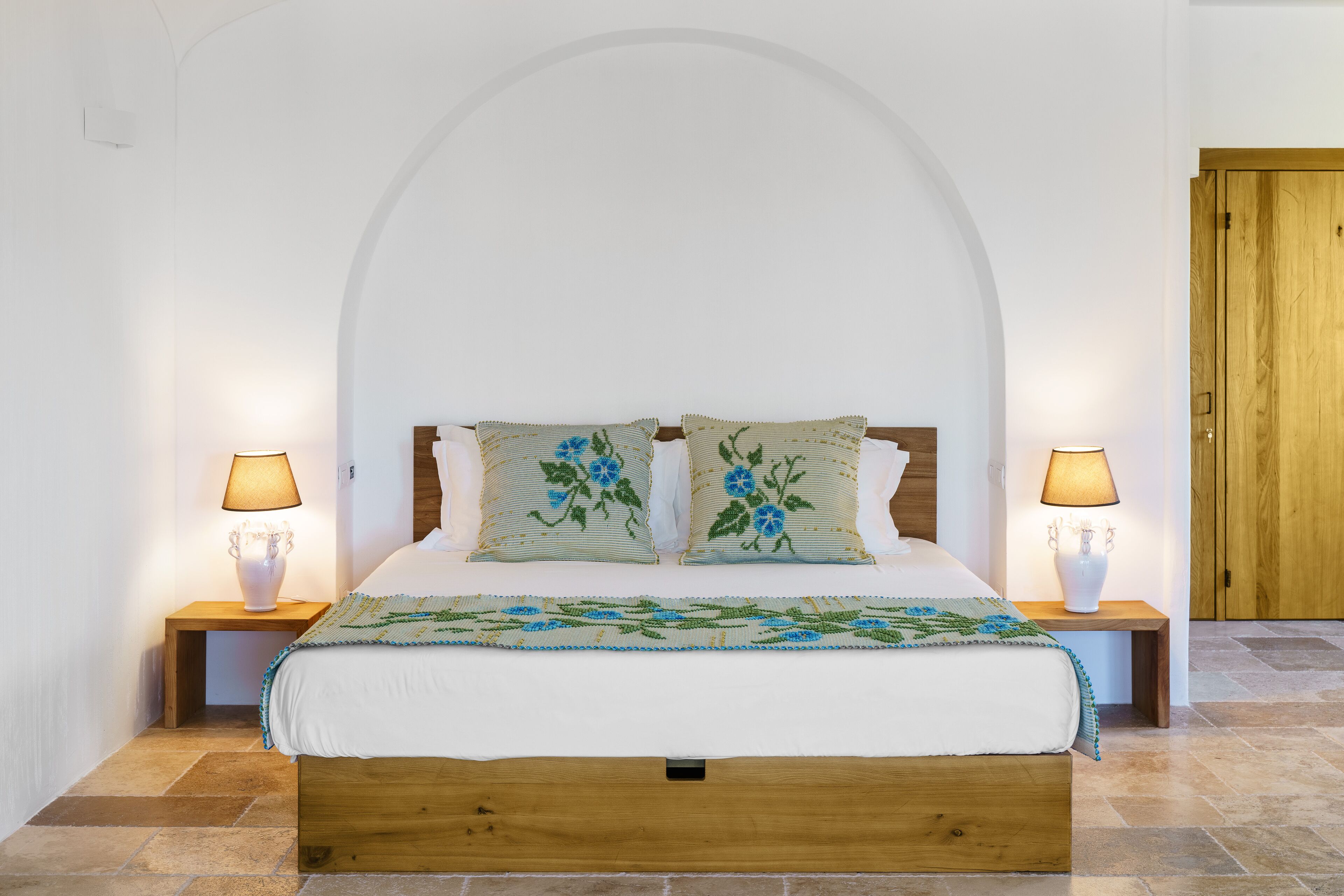 A neatly arranged bedroom with a wooden bed, two bedside lamps, and a floral bedspread.