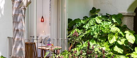 A patio with a wooden chair and table, a door with a hanging light, and lush green foliage.