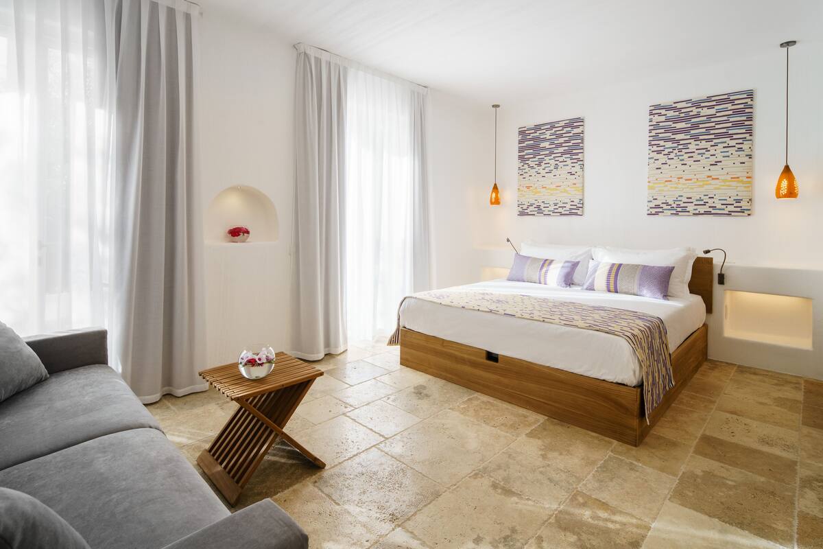A modern bedroom with a large bed, a grey sofa, and two wall-mounted artworks.