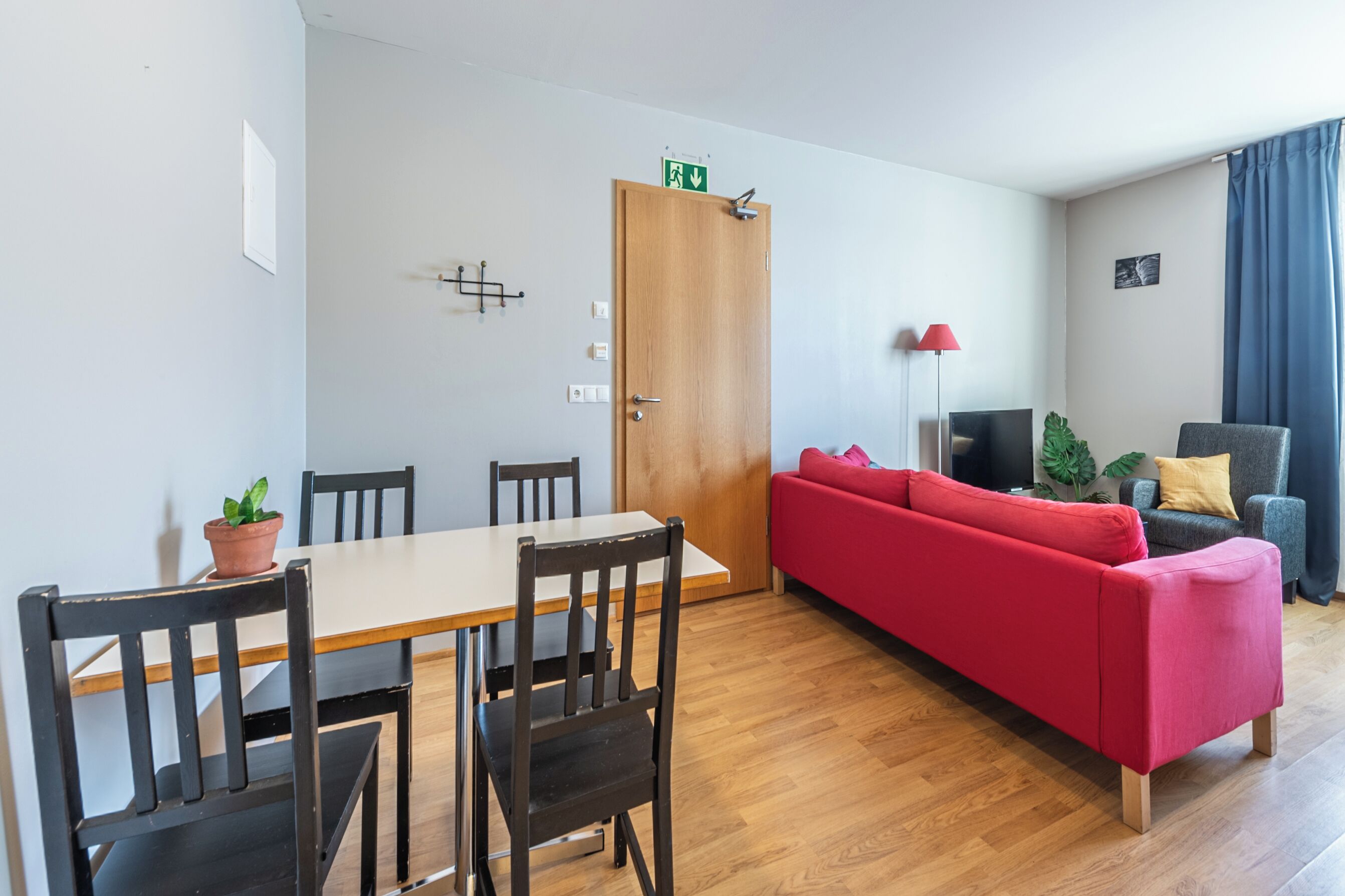 A modern living room with a wooden dining table, red sofa, and a TV.