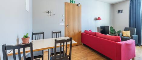 A modern living room with a wooden dining table, red sofa, and a TV.