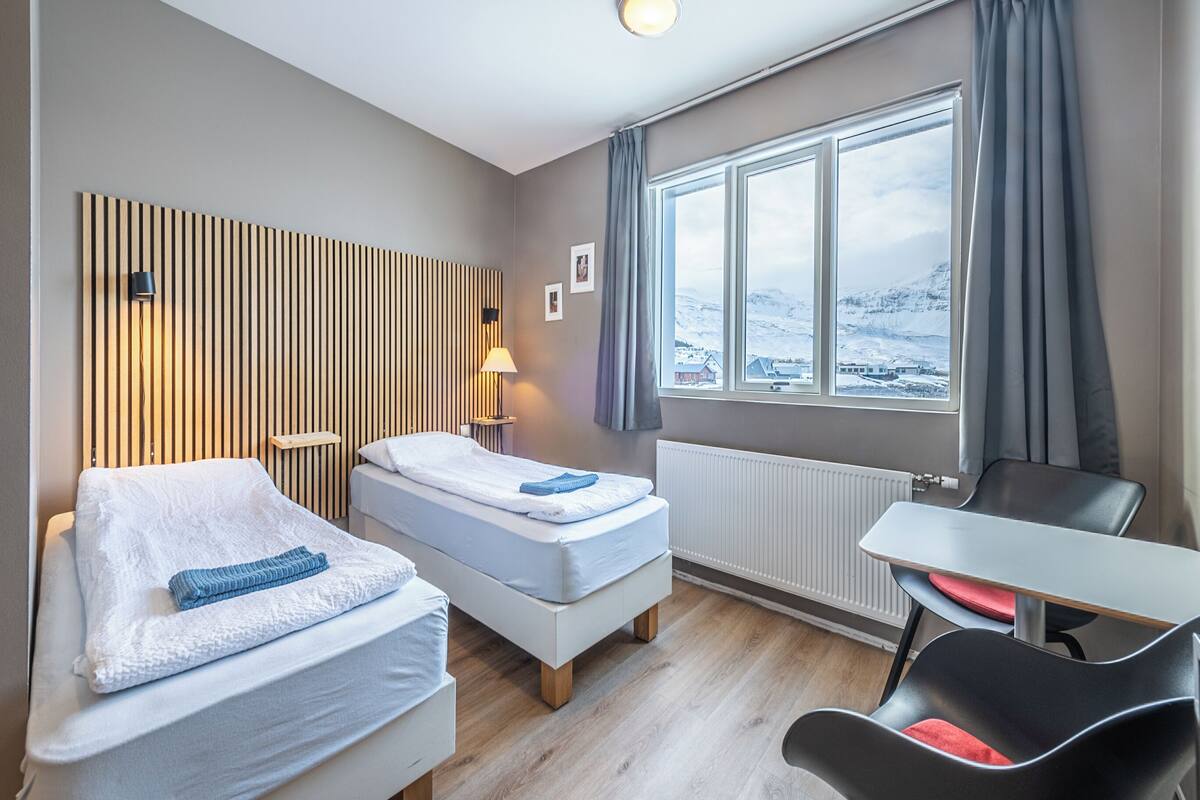 A hotel room with two beds, a desk, and a view of a snowy landscape.
