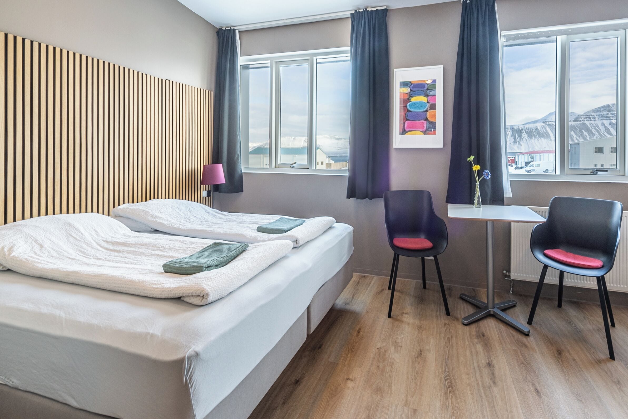 Une chambre d’hôtel avec un lit, deux chaises, une table et une fenêtre avec des rideaux.