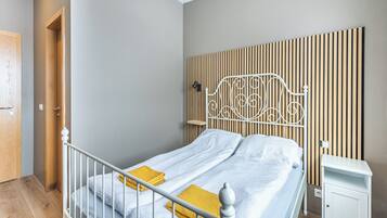 Una cama bien hecha con cabecera metálica blanca, un panel de pared de listones de madera y una mesita de noche con cajón.
