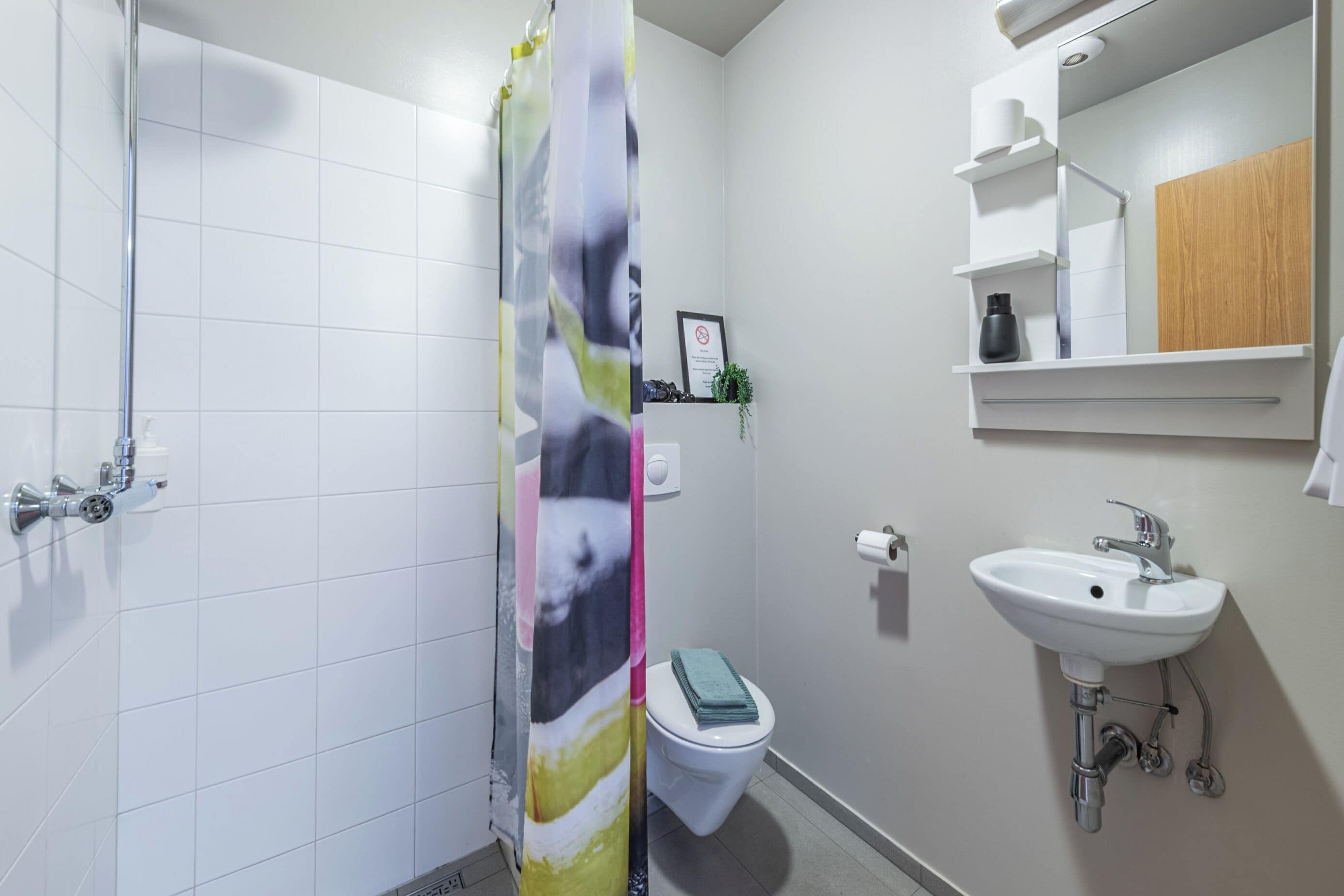 Une salle de bain avec des carreaux blancs, un rideau de douche, des toilettes, un lavabo et un miroir.