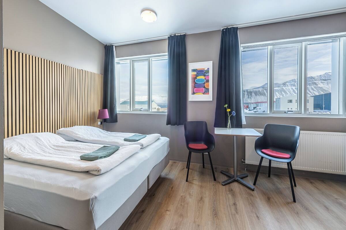 A hotel room with a bed, a desk, a chair, and a window with a view of mountains.