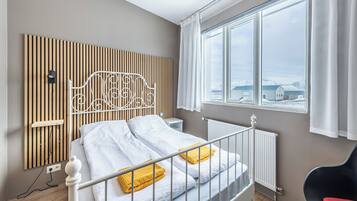 Un dormitorio con cama, ventana con vistas, radiador y mesita de noche.
