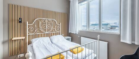 A bedroom with a bed, a window with a view, a radiator, and a bedside table.