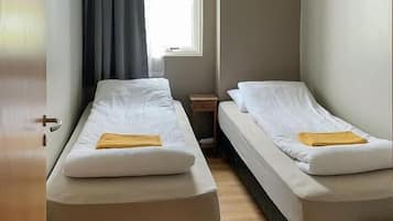 A room with two single beds, a small table, a window with curtains, and a door.