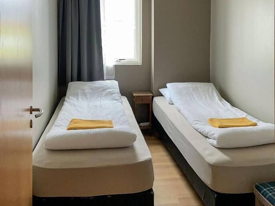A room with two single beds, a small table, a window with curtains, and a door.