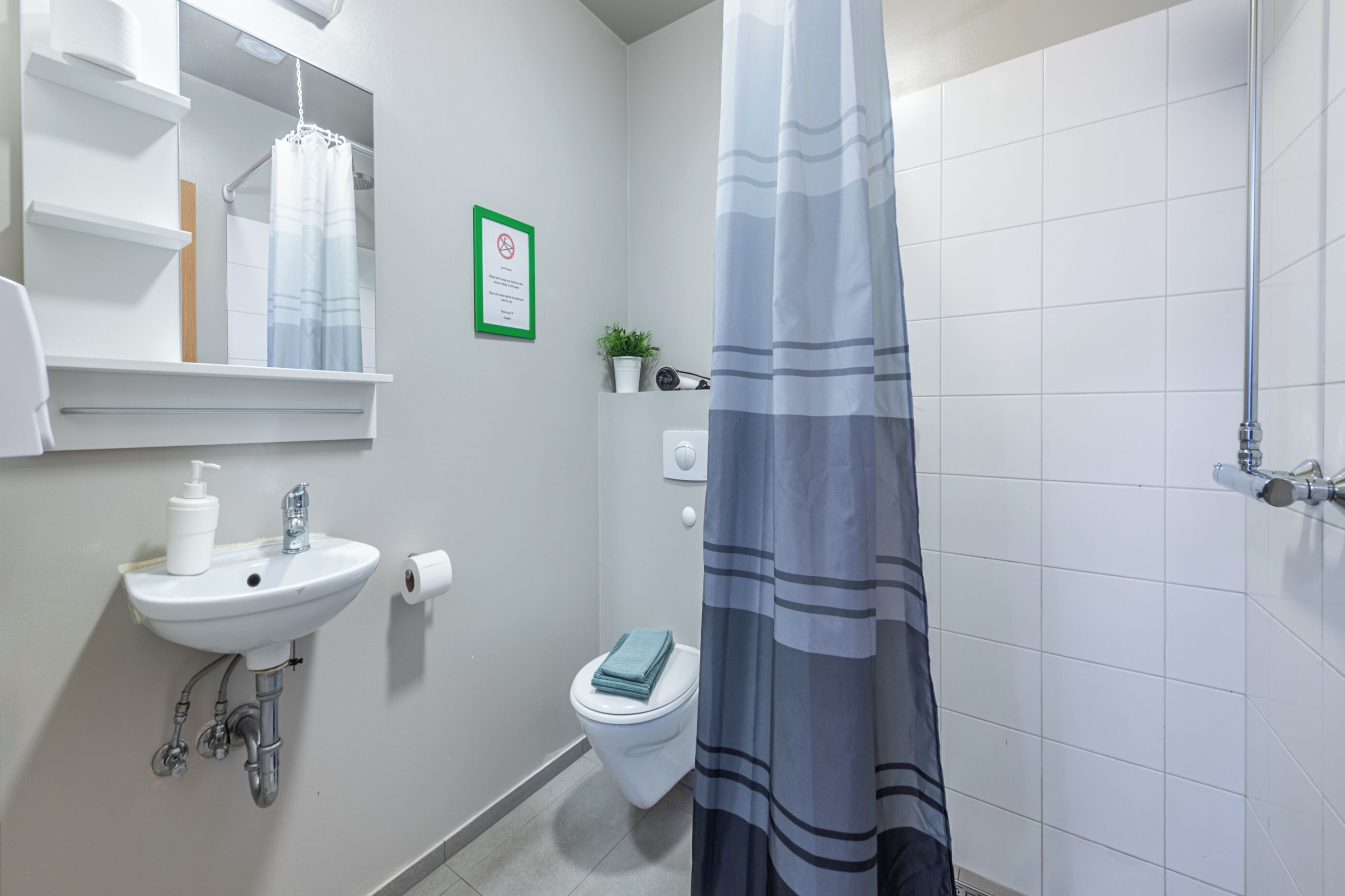 A bathroom with a sink, toilet, shower curtain, and a framed sign on the wall.