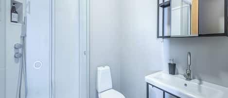 A modern bathroom with a glass shower enclosure, a white toilet, and a sink with a mirror above it.