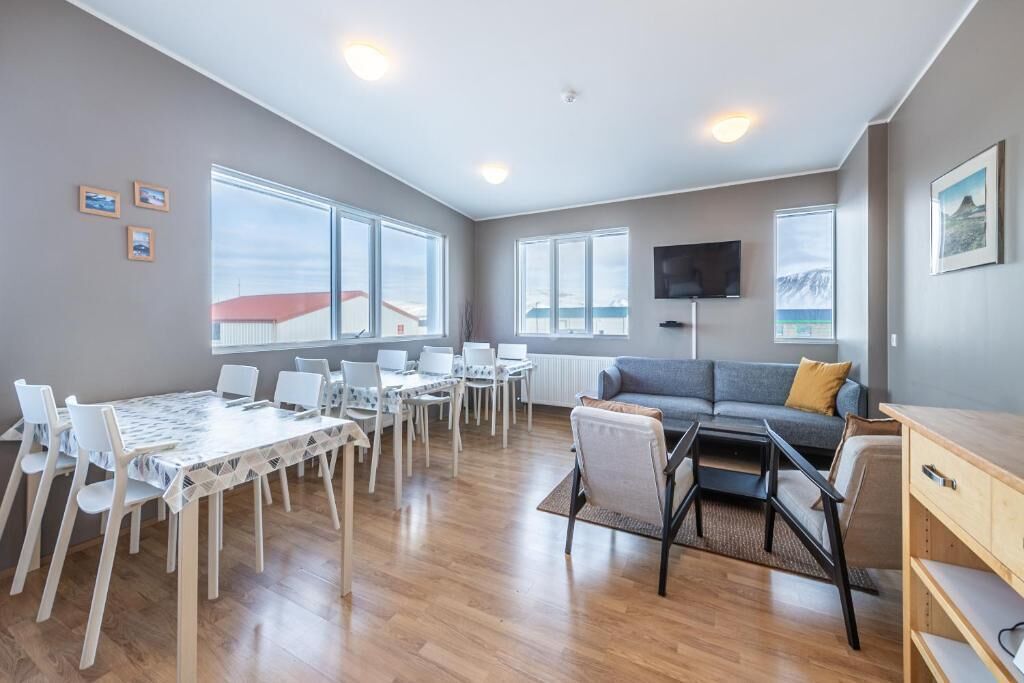 Ein modernes Wohnzimmer mit grauem Sofa, einem Esstisch mit Stühlen, einem an der Wand montierten Fernseher und großen Fenstern mit Blick nach draußen.