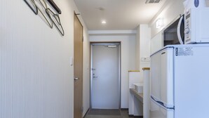 A narrow hallway with a refrigerator and a microwave on the right, a door on the left, and a door at the end of the hallway. - Mr.KINJO in Miegusuku (Naha)