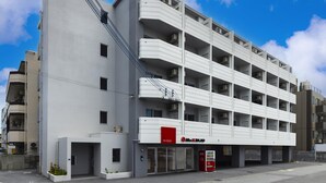 A modern multi-story building with a flat facade, multiple balconies, and a visible commercial space with a red sign. - Mr.KINJO in Miegusuku (Naha)