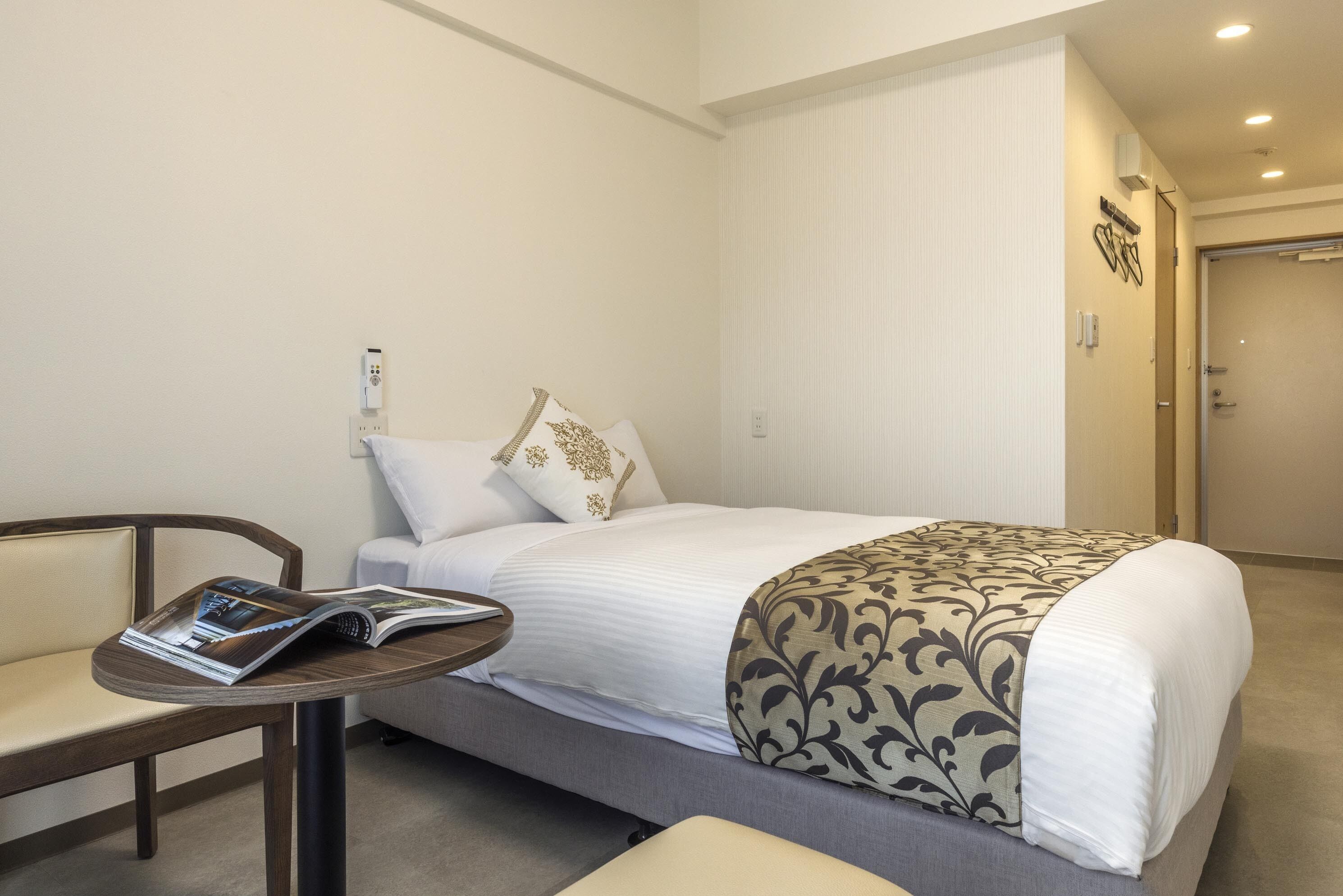 Una habitación de hotel con una cama, una mesita con una revista y una silla.