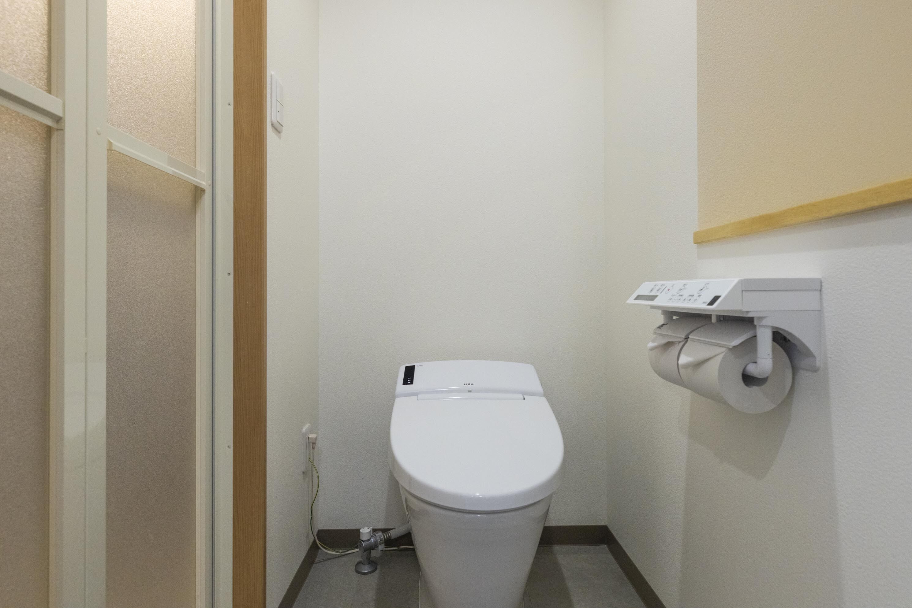 A small, clean bathroom with a white toilet, a toilet paper holder, and a visible pipe.