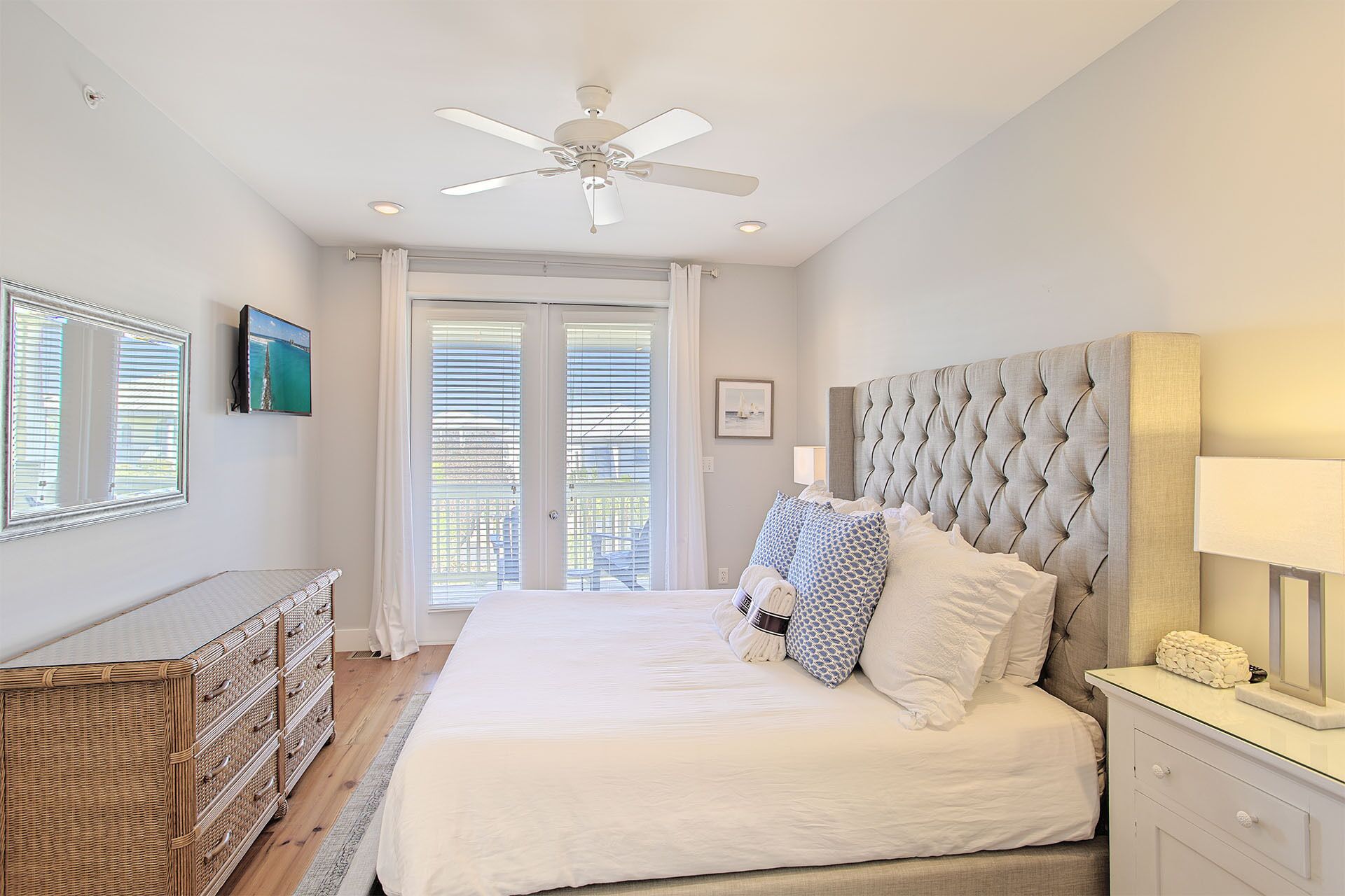 Une chambre avec un grand lit, un ventilateur de plafond, une commode et une fenêtre avec des stores.