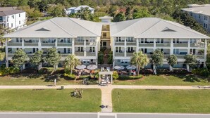 A two-story hotel with a central tower, outdoor seating area with umbrellas, and a view of the surrounding landscape. - Grand Isle 302 - Community Pool, Private Beach Access, 30A, Near Seaside! (Seagrove Beach)