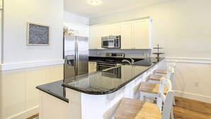 A modern kitchen with white cabinetry, stainless steel appliances, a granite countertop, and a bar area with stools. - Grand Isle 302 - Community Pool, Private Beach Access, 30A, Near Seaside! (Seagrove Beach)