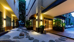 A hotel entrance with a stone pathway leading to the doors, surrounded by potted plants and a gravel area. - Ji Hotel (xi'an Giant Wild Goose Pagoda East Xiaoz (Xi'an)