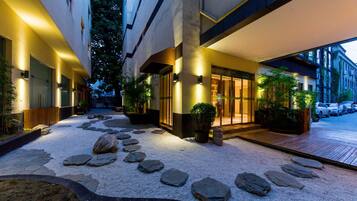 Entrada de hotel con un camino de piedra que lleva a las puertas, rodeada de plantas en macetas y un área de grava.