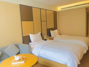 A hotel room with two beds, a sofa, a small round table with a teapot, and a wall panel design. - Ji Hotel (xi'an Giant Wild Goose Pagoda East Xiaoz (Xi'an)