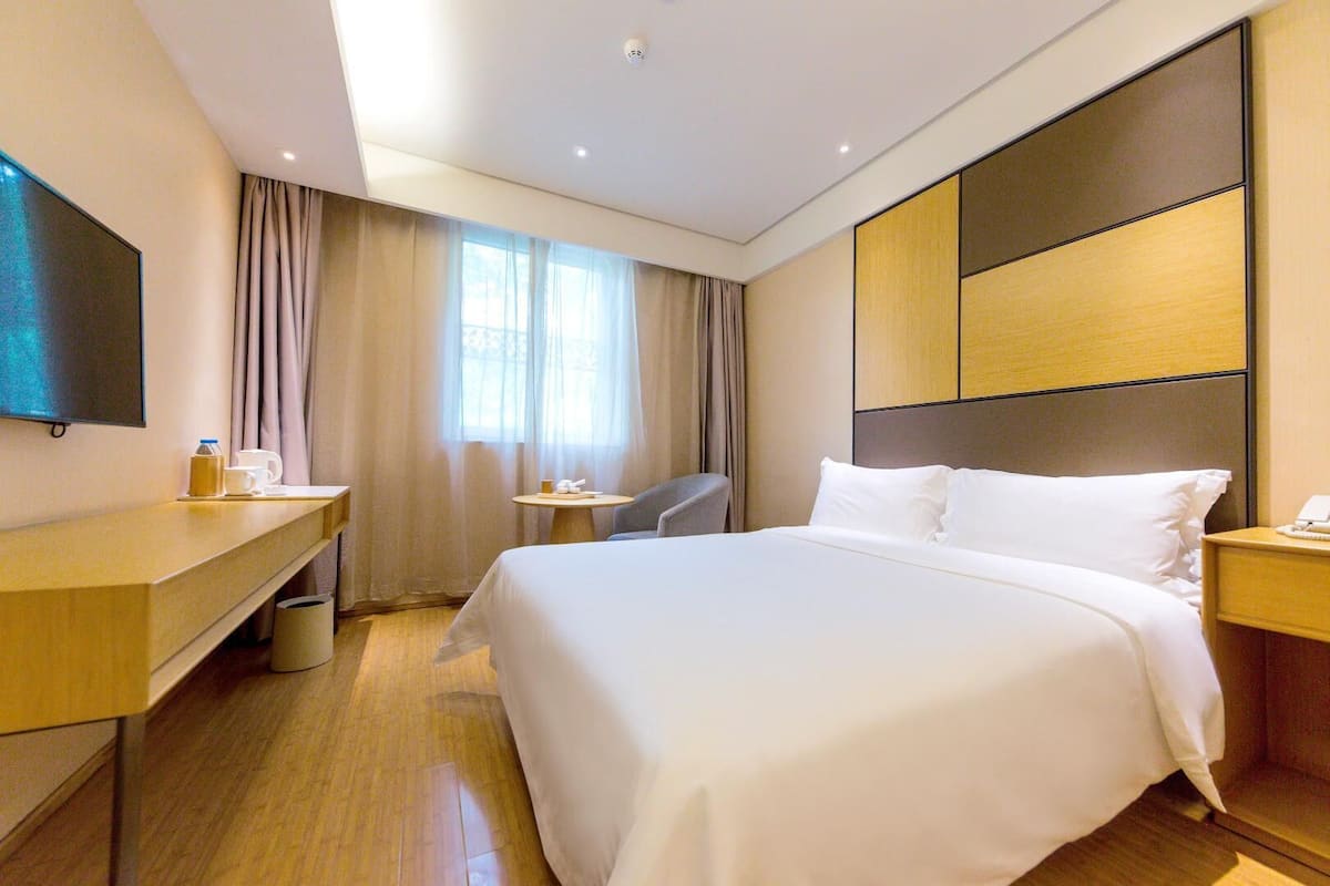 Une chambre d’hôtel avec un grand lit, un bureau avec une chaise, une télévision et une petite table sur laquelle se trouvent un téléphone et une tasse.