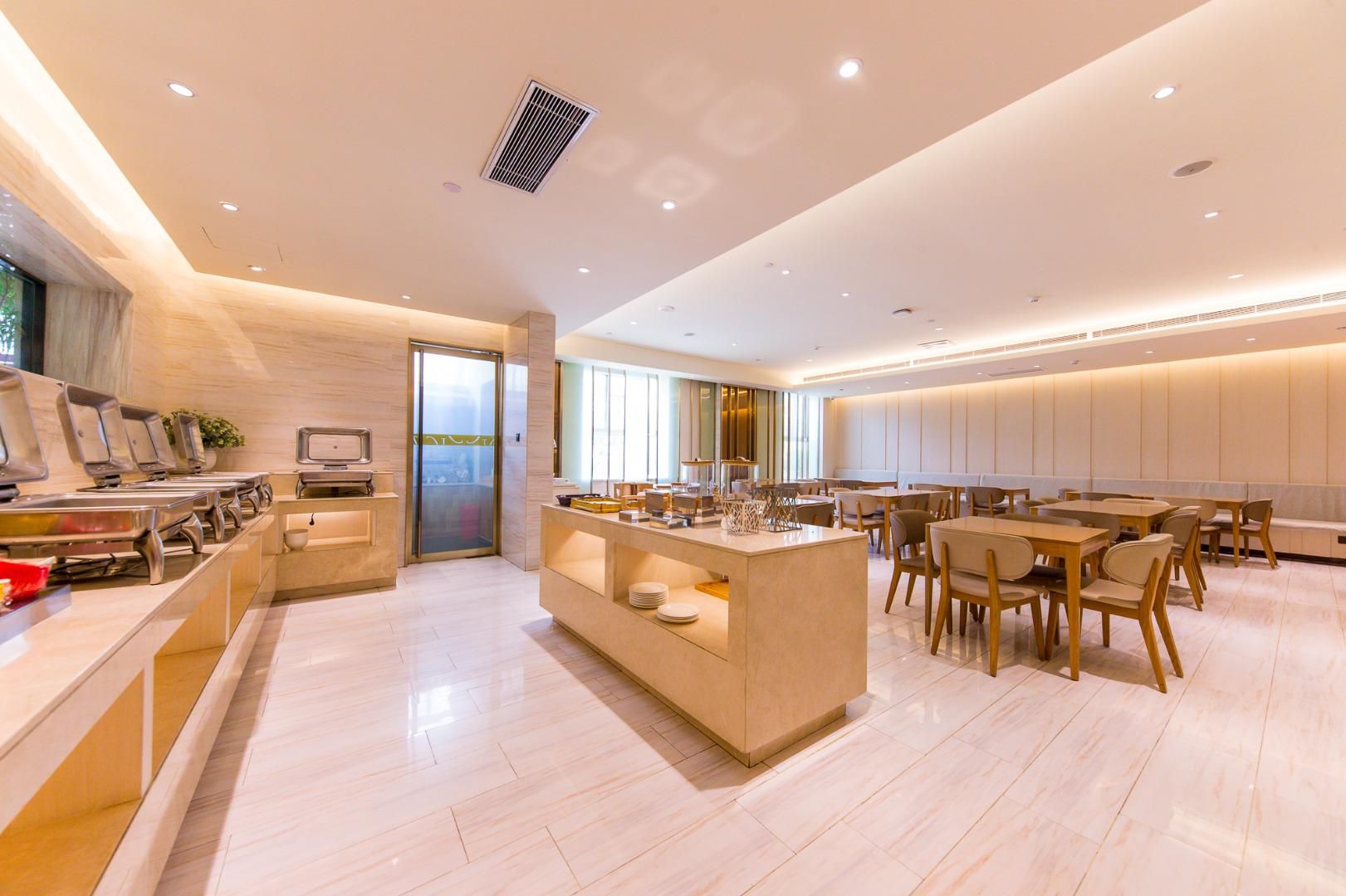 Comedor de hotel moderno con una isla central, disposición de mesas y sillas, y vista a través de un ventanal.