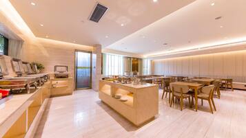 Comedor de hotel moderno con una isla central, disposición de mesas y sillas, y vista a través de un ventanal.
