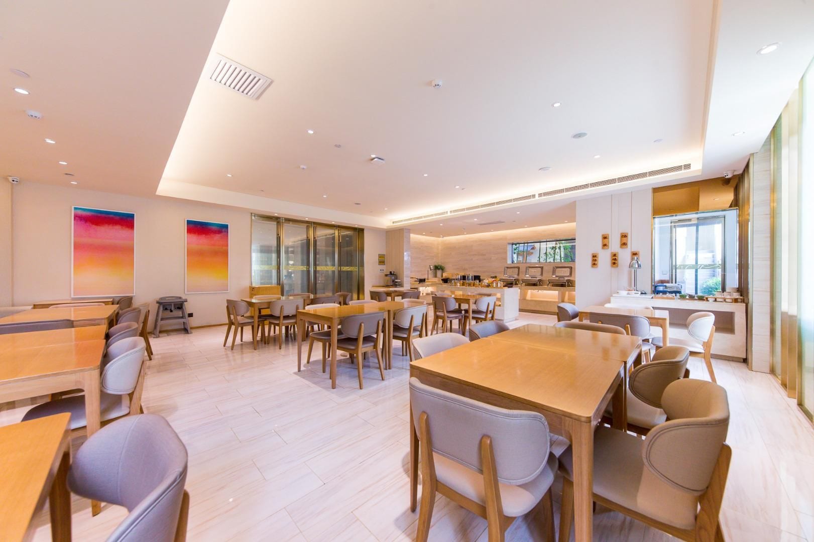 A modern dining area with multiple tables and chairs, a kitchen in the background, and large windows.