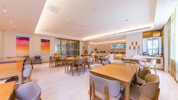 A modern dining area with multiple tables and chairs, a kitchen in the background, and large windows.