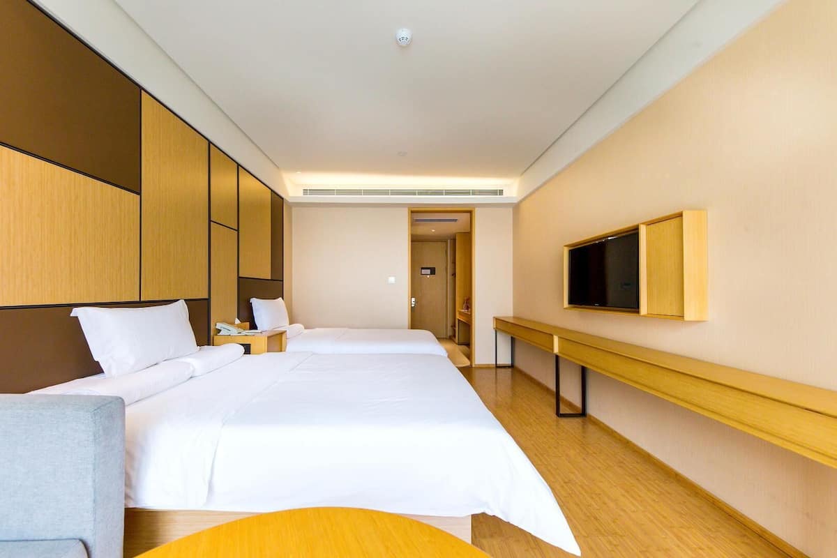 Une chambre d’hôtel avec deux lits, une télévision, un bureau et une salle de bain que l’on aperçoit à l’arrière-plan.