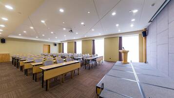 A conference room with rows of tables and chairs, a podium, and a projector screen.
