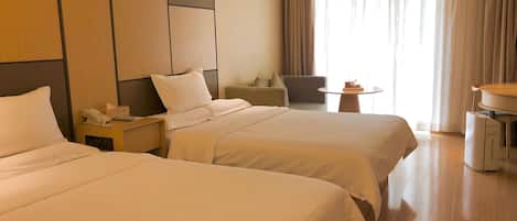A hotel room with two beds, a desk, a chair, a small table, and a large window with curtains.