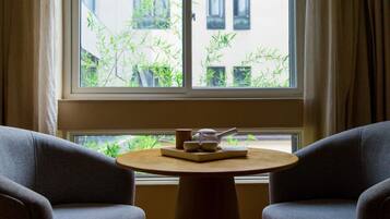 A room with a round wooden table, two grey armchairs, and a window with bamboo plants outside.