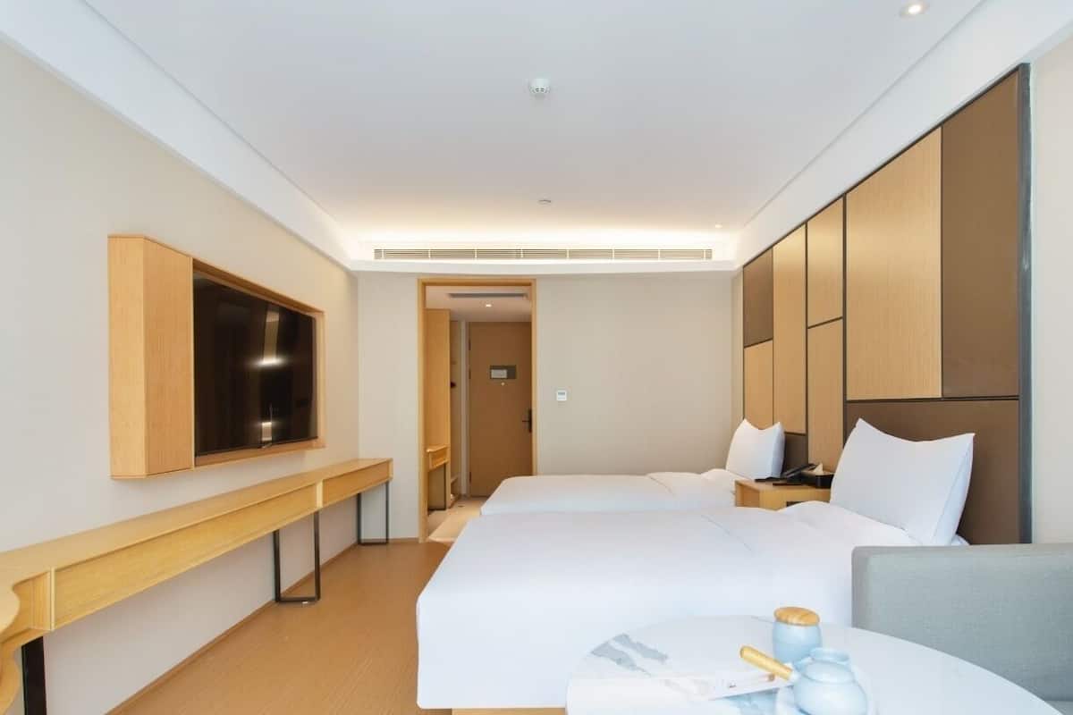 Une chambre d’hôtel avec deux lits, une télévision, un bureau et une petite table sur laquelle se trouvent une tasse et un livre.